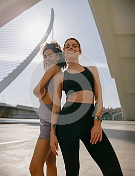 Two young female sportswomen have a rest after morning jogging standing outdoors and looks camera