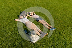 Two young female students with backpacks lying on green lawn grass