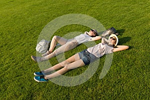 Two young female students with backpacks lying on green lawn grass. Top view, side view.