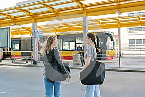 Two young female students at a bus stop in a modern city