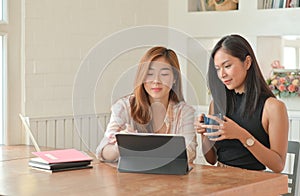 Two young female students with coffee are using a laptop to study online at home in the summer semester