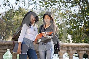 Two young female students in the street looking at their notebooks