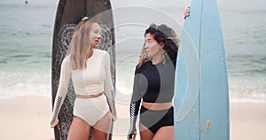 Two young female surfers talking on the beach next to their surfboards.