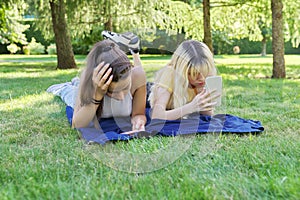 Two young female teenagers lying on grass in park with smartphones