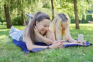 Two young female teenagers lying on grass in park with smartphones