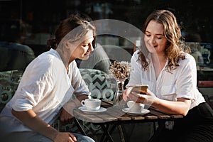 Two young females using smartphone in a cafe outdoors sitting in a cafe with coffee