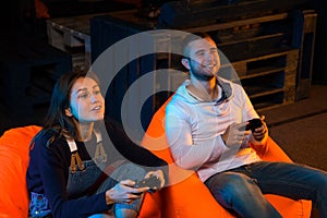Two young gamer sitting on poufs and playing video games together