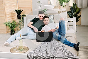 Two young gay men lying on the bed and using a laptop. Handsome gay men spending time together. Homosexual couple, gay