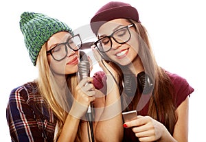 Two young girl friends standing together and listening to music and singing