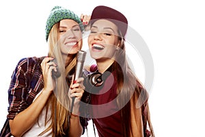 Two young girl friends standing together and listening to music and singing