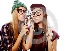 Two young girl friends standing together and listening to music and singing