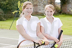 Two young girl friends on tennis court smiling