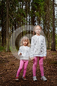 Two young girl playing and having fun together on walk in forest outdoors. Happy loving family with two sisters or female friends