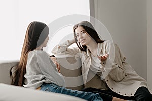 Two young girlfriends talking, sitting on couch