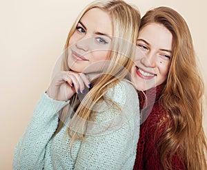 Two young girlfriends in winter sweaters indoors having fun. Lifestyle. Blond teen friends close up