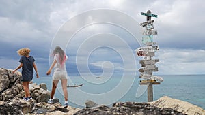 Two young girls argue and choosing which way they should go. wooden sign post arrows pointing to various cities and