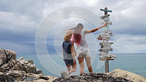 Two young girls argue and choosing which way they should go. wooden sign post arrows pointing to various cities and