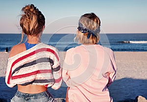 Two young girls, best friends sitting together on the beach at s