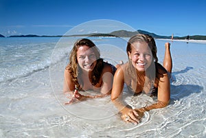 Two young girls in bikini laying in the water