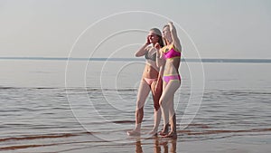 Two young girls in bikinis on the beach walk