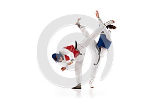 Two young girls in dobok and helmet training, practicing taekwondo poses, stances isolated over white background