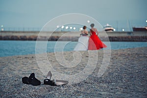 Two young girls in fashionable dresses walking at sandy beach without shoes evening time. Teens together outside at the beach