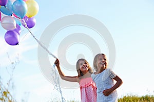 Two Young Girls Holding Bunch Of Colorful Balloons Outdoors