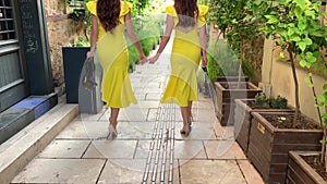 Two young girls with long dark hair are holding violins in their hands and walking down the historical street of old town of