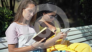 Two young girls look at a mobile phone and then start reading a book.