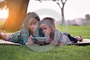 Two young girls lying on the lawn looking at their phones, summer, golden hour, sunset. SSTKHome