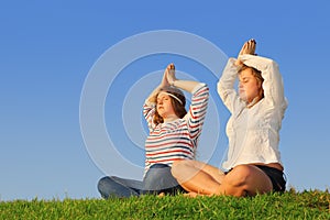 Two young girls meditate at green grass