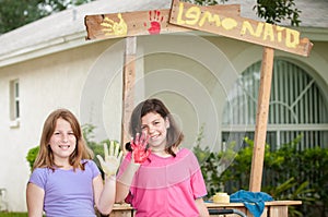 Two young girls painting a lemonade stand sign