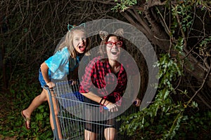 Two Young Girls Playing in a Shopping Cart Under an Overgrown Me