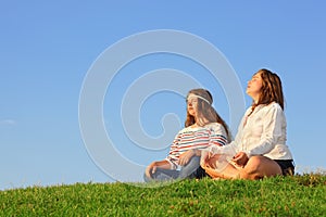Two young girls sit and meditate at green grass