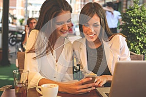 Two young girls sitting in cafe using smart phone. Girl showing