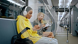 Two young girls sitting in modern metro, listening to music in headphones.
