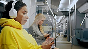 Two young girls are sitting in modern metro, looking at phones, listening music