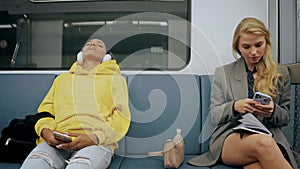 Two young girls are sitting in modern metro train after work, looking at phones