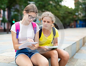Two young girls sitting in park and doing homework