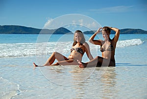 Two young girls sitting in water at beach