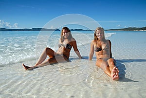 Two young girls sitting in water at beach