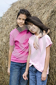 Two young girls standing by haybale