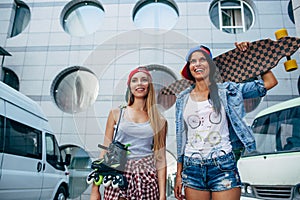 Two young girls standing with longboard and roller skates