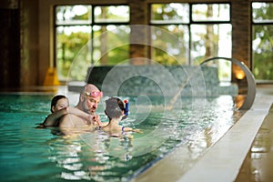 Two young girls and their father having fun in indoor pool. Child learning to swim. Kid having fun with water toys. Family fun in