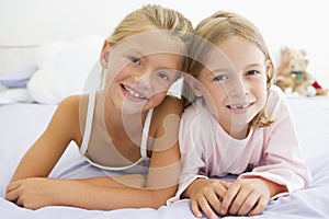 Two Young Girls In Their Pajamas Lying On A Bed