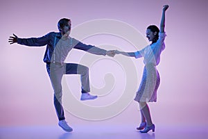 Two young graceful dancers, man and woman in vintage style outfits dancing rock-and-roll isolated on lilac color