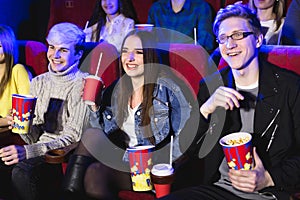 Two young guys and a girl watching a Comedy in a movie theater. Young friends watch movies in the cinema. Group of