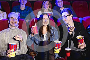 Two young guys and a girl watching a Comedy in a movie theater. Young friends watch movies in the cinema. Group of