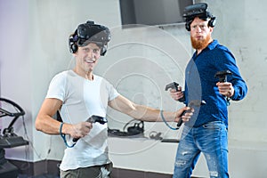 Two young guys are playing in a shooter, in virtual reality glasses