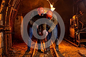 Two young guys in a working uniform and protective helmets, carry out work in the mine